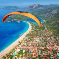 Paragliding in the sky. Paraglider tandem flying over the sea with blue water and mountains in bright sunny day. Aerial view of paraglider and Blue Lagoon in Oludeniz, Turkey. Extreme sport. Landscape