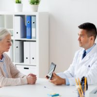 medicine, age, healthcare and people concept - senior woman doctor showing tablet pc computer to senior woman patient at hospital