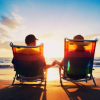 senior couple of old man and woman sitting on the beach watching sunset